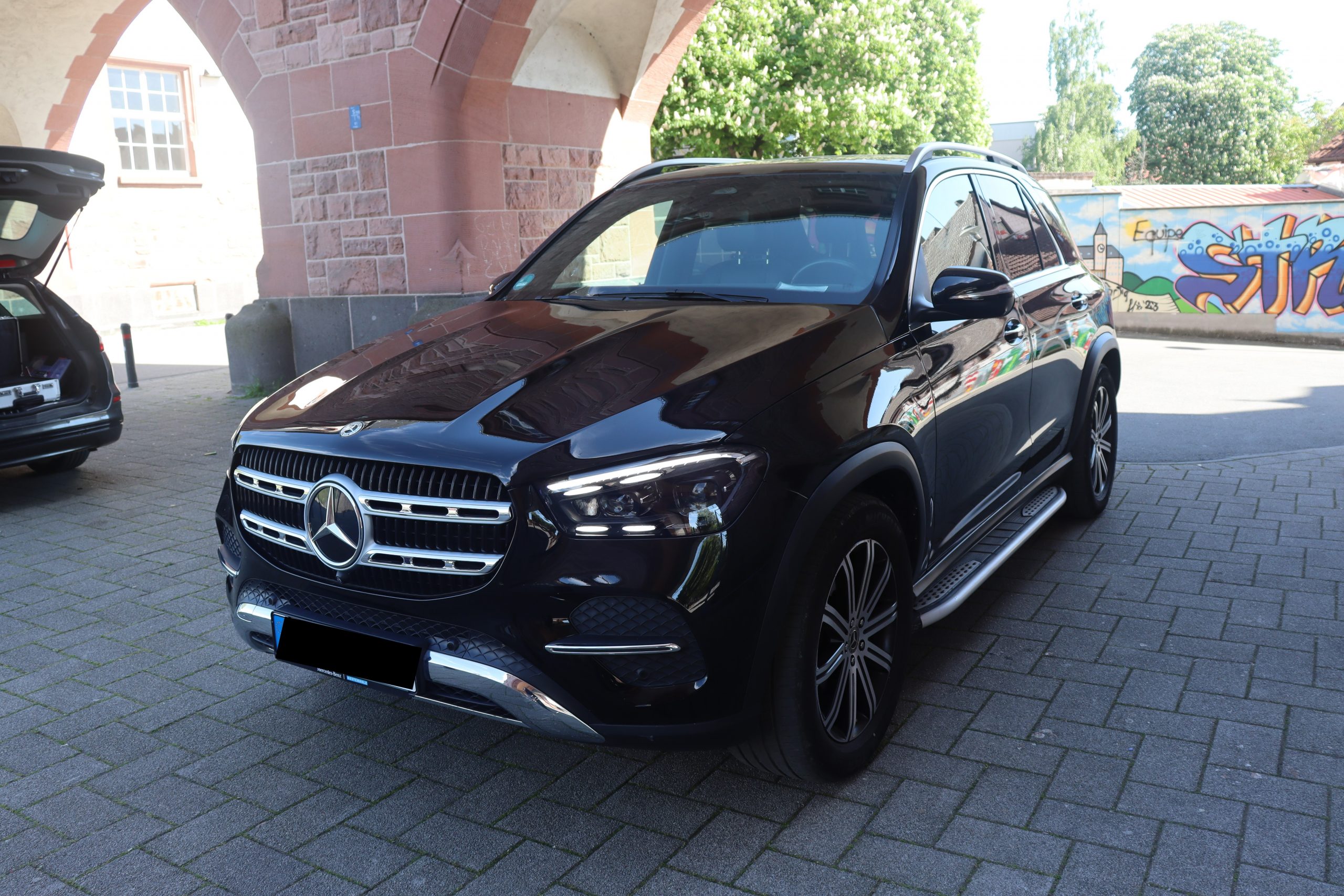 Luxuriöser schwarzer SUV parkt vor einem Backsteingebäude mit Wandgemälde im Hintergrund bei sonnigem Wetter.
